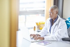 mature female doctor sitting at a desk typing on a laptop