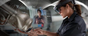 person wearing AR headset while working on a piece of machinery. Another person is on a screen observing.