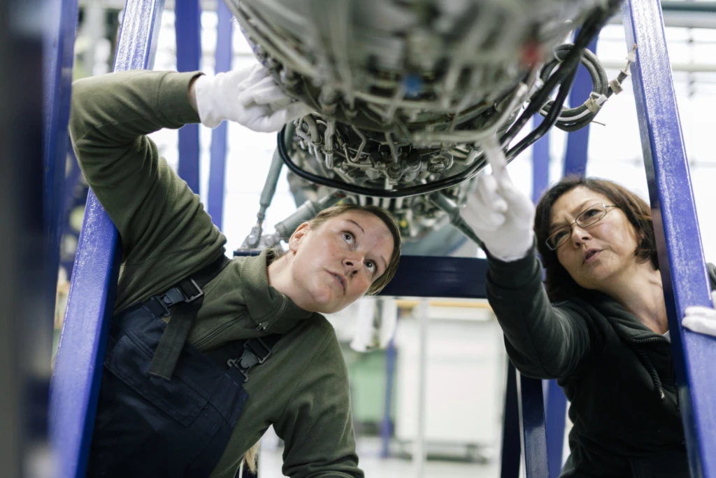Female mechanics examine an aircraft engine.