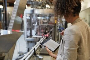 Adult female in an industrial factory setting holding a platinum Microsoft Surface Pro 7 in tablet mode while preparing to use a Microsoft Surface Pen with Microsoft Dynamics screen shown