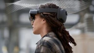Head of a young woman looking to the left, wearing a Hololens 2 mixed reality device, in a manufacturing environment.