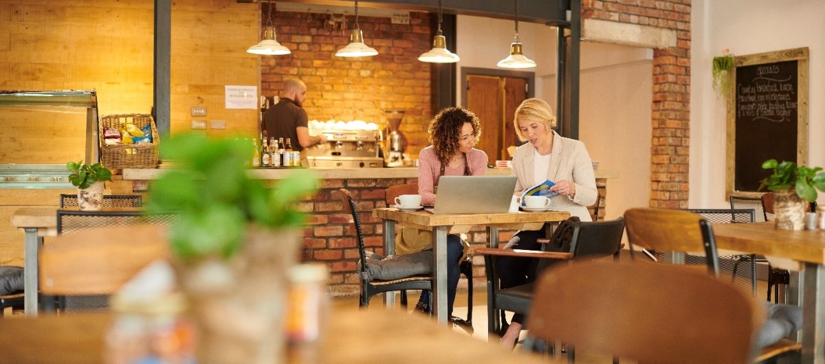 Interior: warmly lit exposed brick cafe. Financial advisor sits with new business owner.