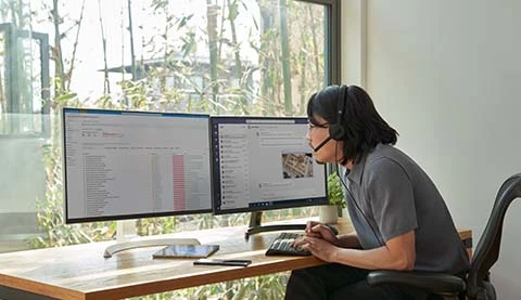 Ein Mann sitzt mit Headset im Home-Office vor zwei Bildschirmen.