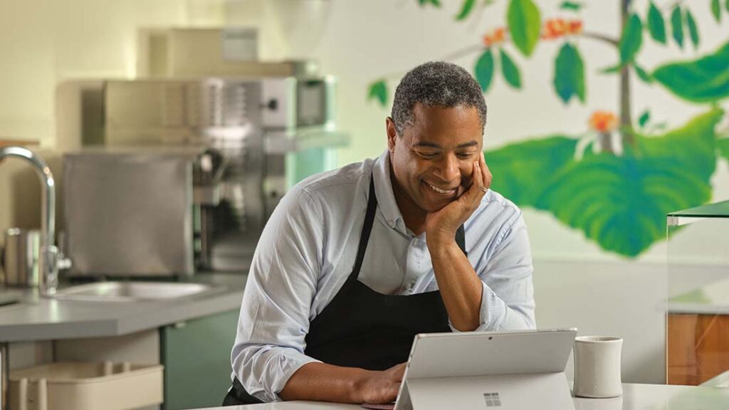 Mann in einer Kochschürze steht in einer Restaurantküche und blickt auf ein Surface Laptop Pro