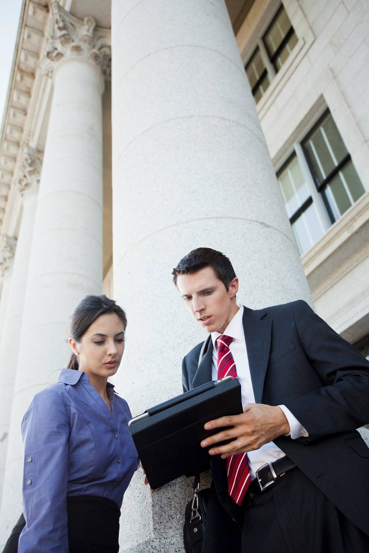 Two business people looking at a tablet on the steps of a building