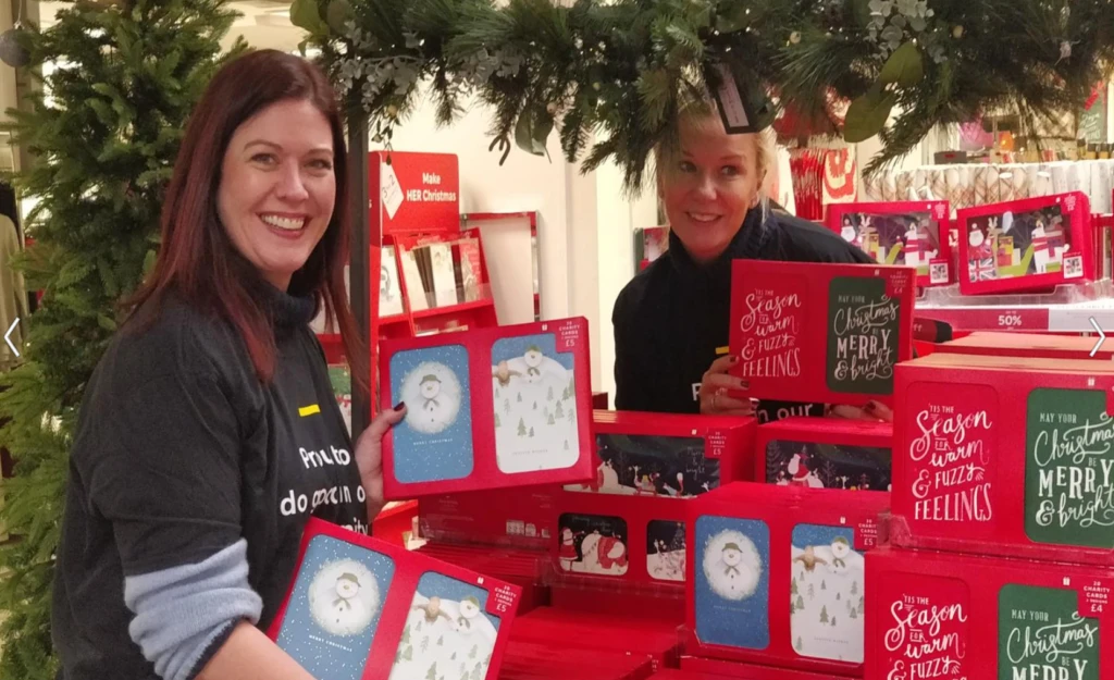 Two smiling women stocking boxes of Christmas cards in a store