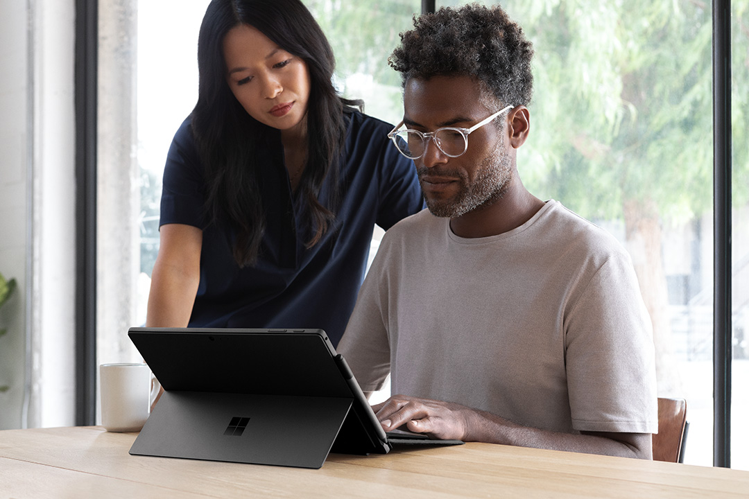 Man and woman collaborating while working on Black Surface Pro 6 inside office
