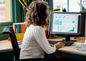 Female employee working on Dynamics 365 presentation of charts and graphs on a Surface Studio monitor.
