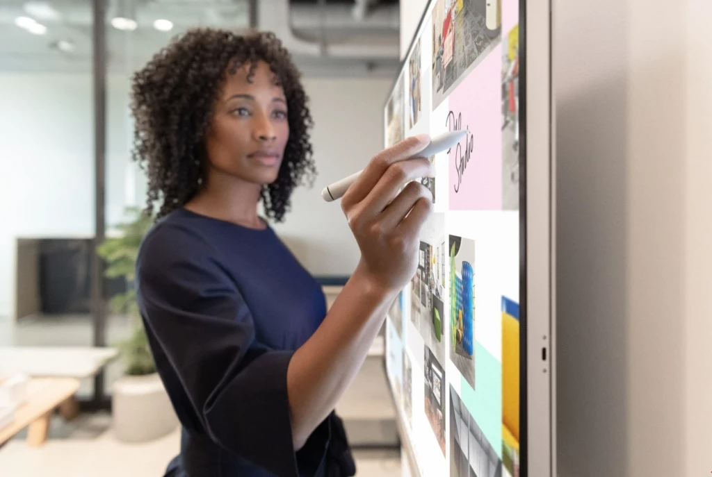 A woman uses a Surface Hub 2S to brainstorm. The hybrid workplace could see the traditional office transform into creative, brainstorming areas.