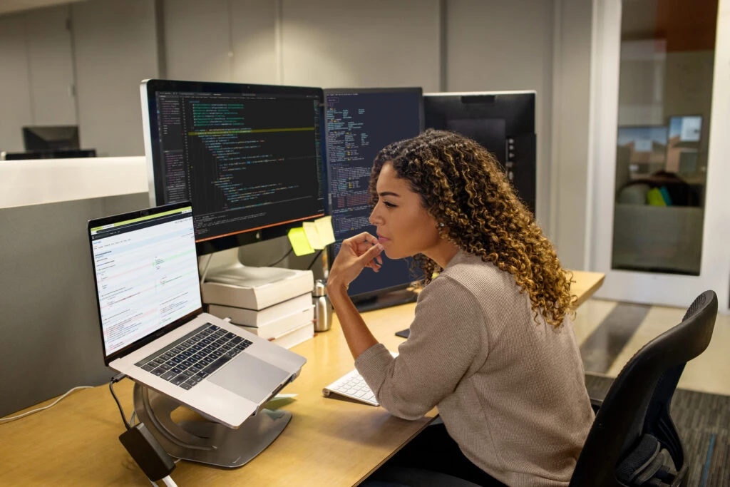 Developer working at enterprise office workspace. Focused work. She has customized her workspace with a multi-monitor set up.