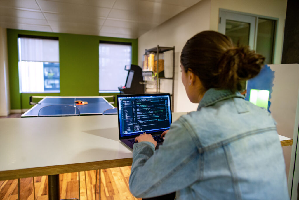 Female developer working on the go from the office breakroom or kitchen. Empty ping pong table in the background.