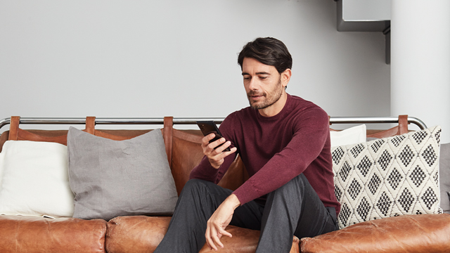 Man sitting on the couch looking down at the phone he is holding.