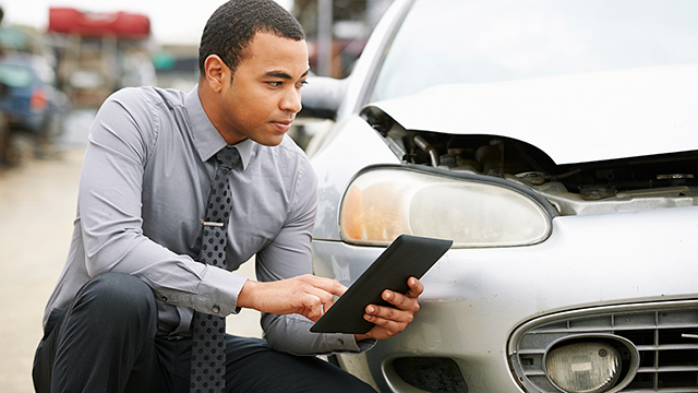 Car salesman crouching next to a car using a tablet