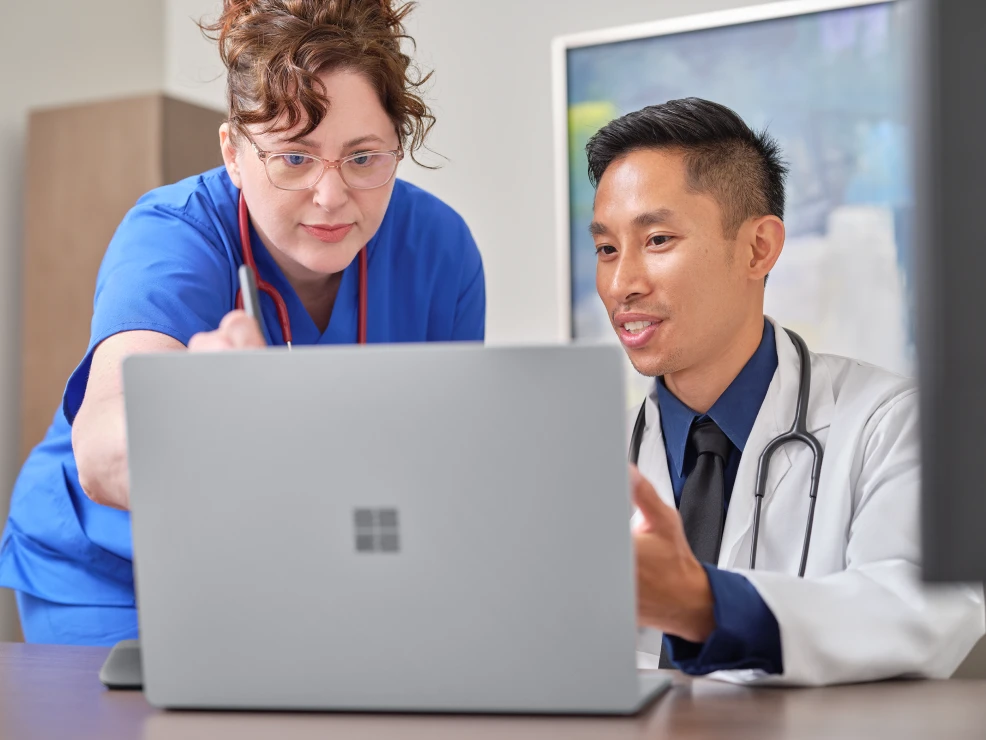 Two medical professionals talking about something on a laptop screen in front of them.