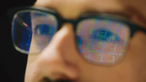 a close up of a man's face who is wearing glasses. The glasses have lines of code reflected.