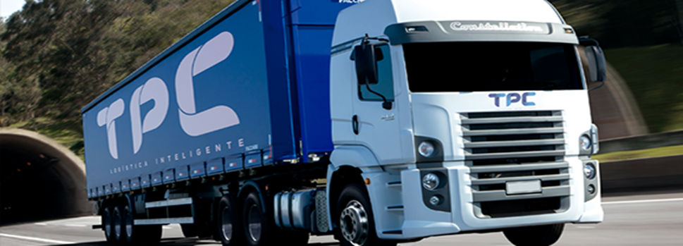 A semitruck with a white cab and blue container with T P C in white letters. The truck is emerging from a tunnel.