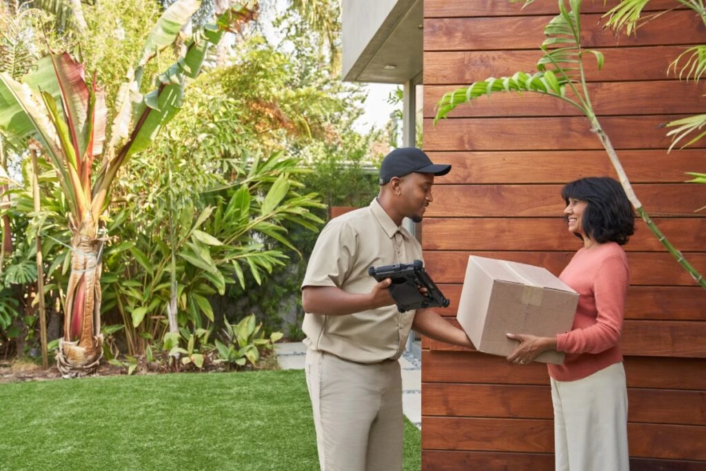 Delivery person handing a package to a satisfied customer at the customer’s doorstep. Keywords: Dynamics 365; purchase; online ordering; ecommerce; delivering a box; Surface tablet; at home; receiving an order; driver; man; woman
